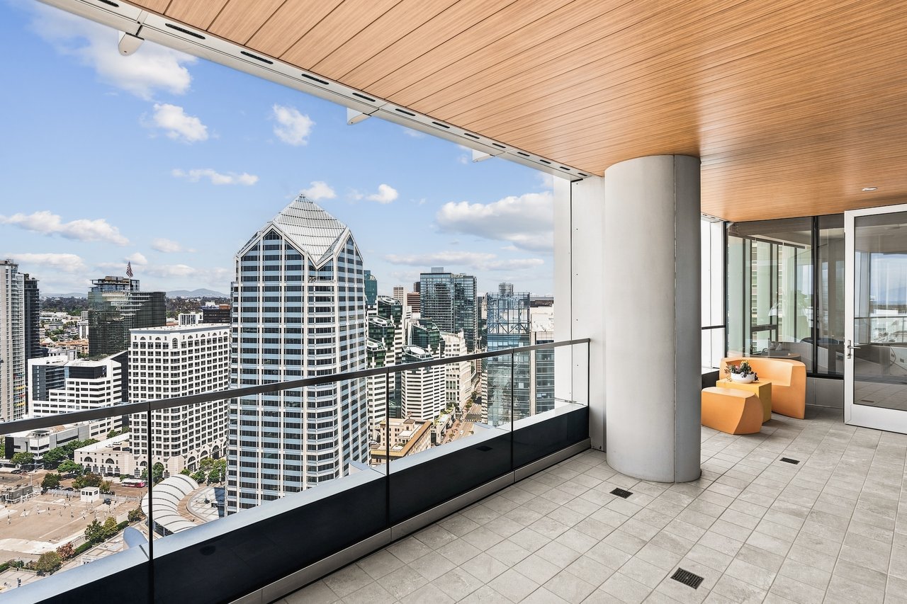 High-rise balcony with orange lounge chairs and a glass railing overlooking downtown San Diego.