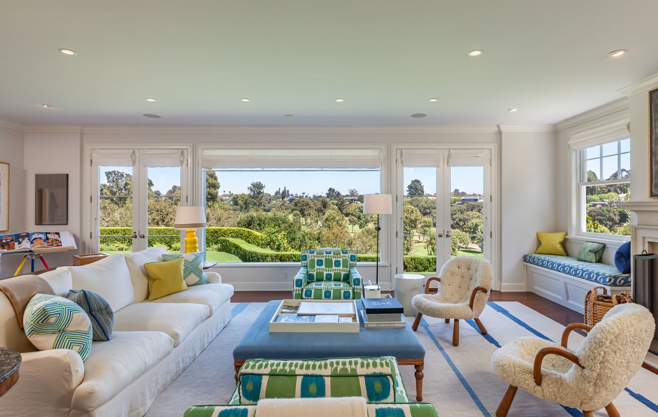 Living room with white sofas and colorful chairs overlooking green golf course grounds.