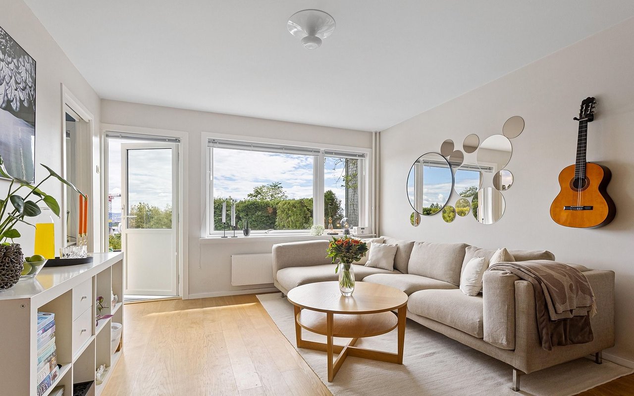 Bright living room with a beige sectional, large windows, and a guitar mounted on the wall.