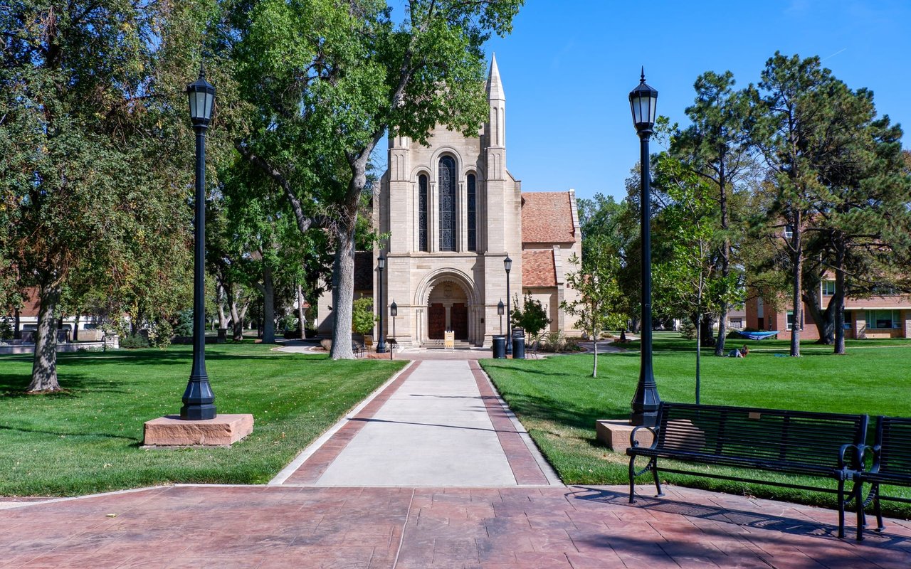 A grand stone chapel with a pathway leading to its entrance, surrounded by a green lawn and street lamps.