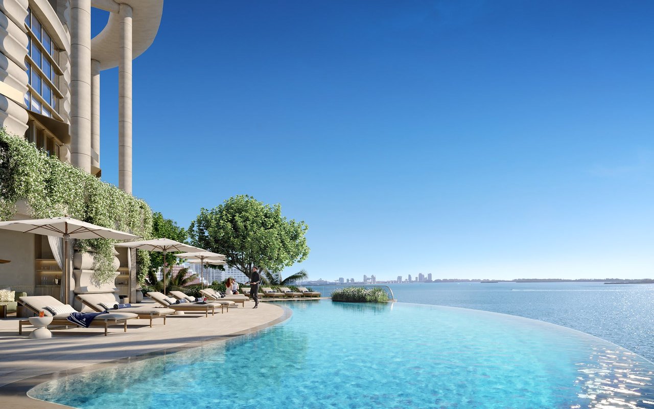 Luxury residence pool terrace overlooking the water and distant Miami skyline, with loungers and umbrellas.