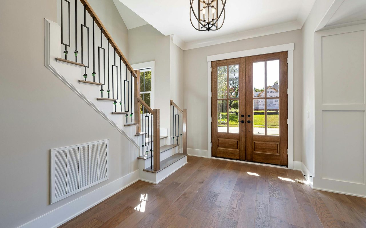 An entrance with wooden stairs, flooring, a door, light walls, and a chandelier overhead.