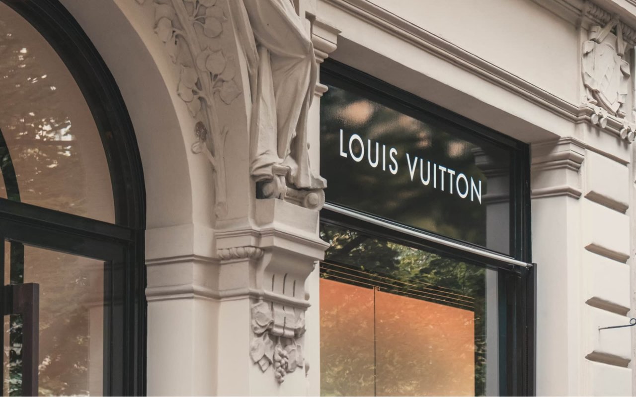 Luxury Louis Vuitton store facade with arched doorway, lit window display, on a busy street.