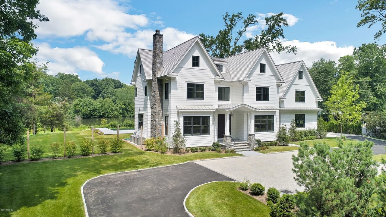 A luxurious estate with a white mansion, a swimming pool, and tennis courts in Greenwich, Connecticut.