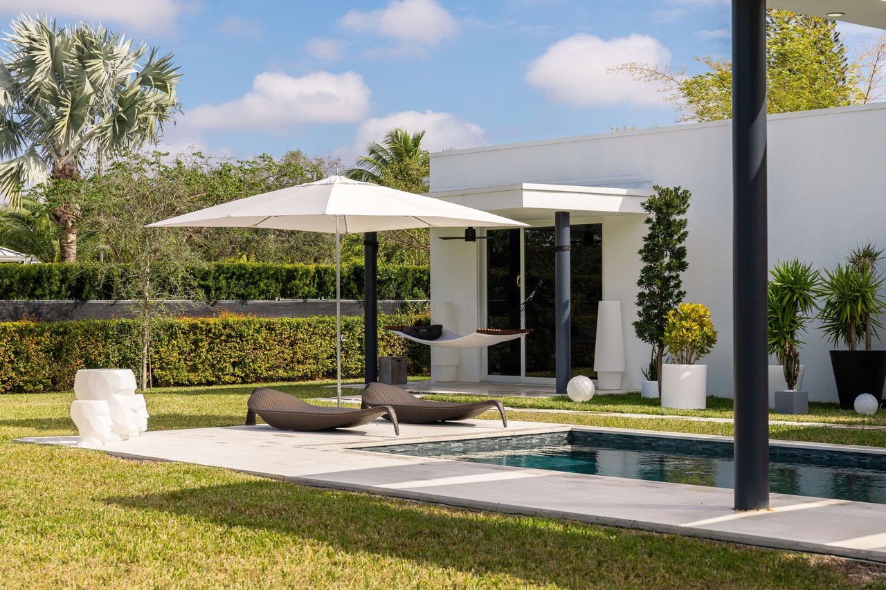  Beyond the pool, a white contemporary house with large glass doors is visible