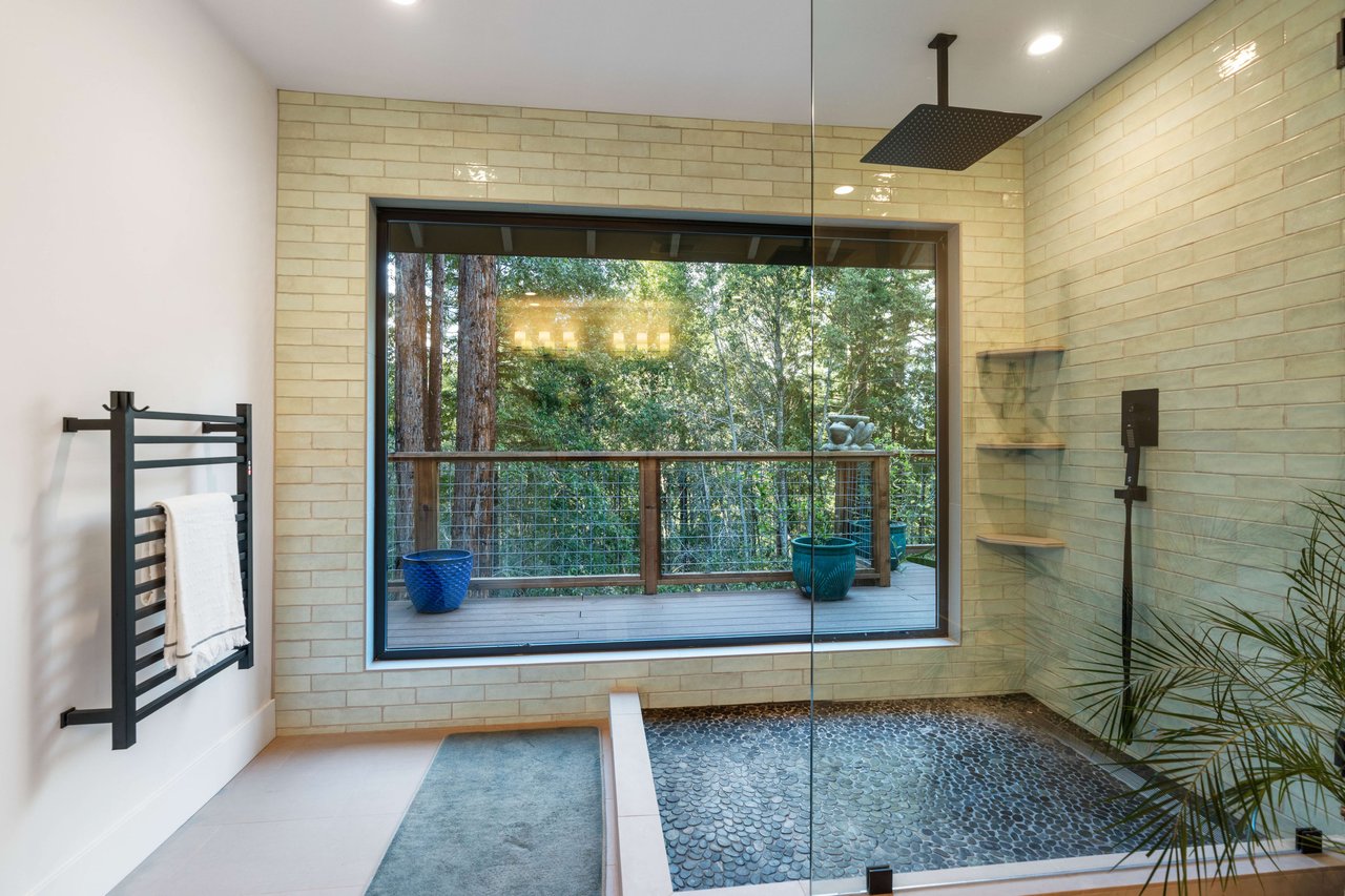 Modern tiled bathroom with a pebble-floor shower and a large window overlooking trees.