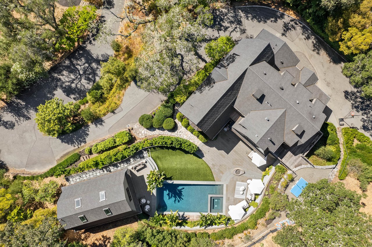 Aerial view of a large estate featuring a rectangular pool, spacious patio, and landscaped garden.