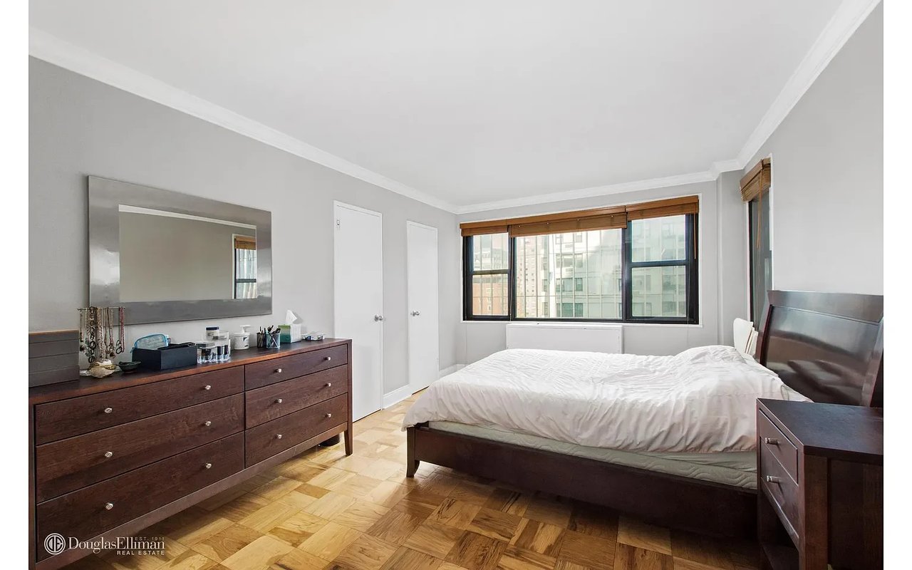 Bedroom with a dark wood bed, matching dresser, parquet flooring, and wide windows.