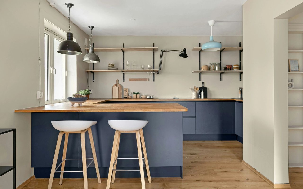 Modern kitchen with navy cabinets, wood countertops, open shelving, and two white bar stools.