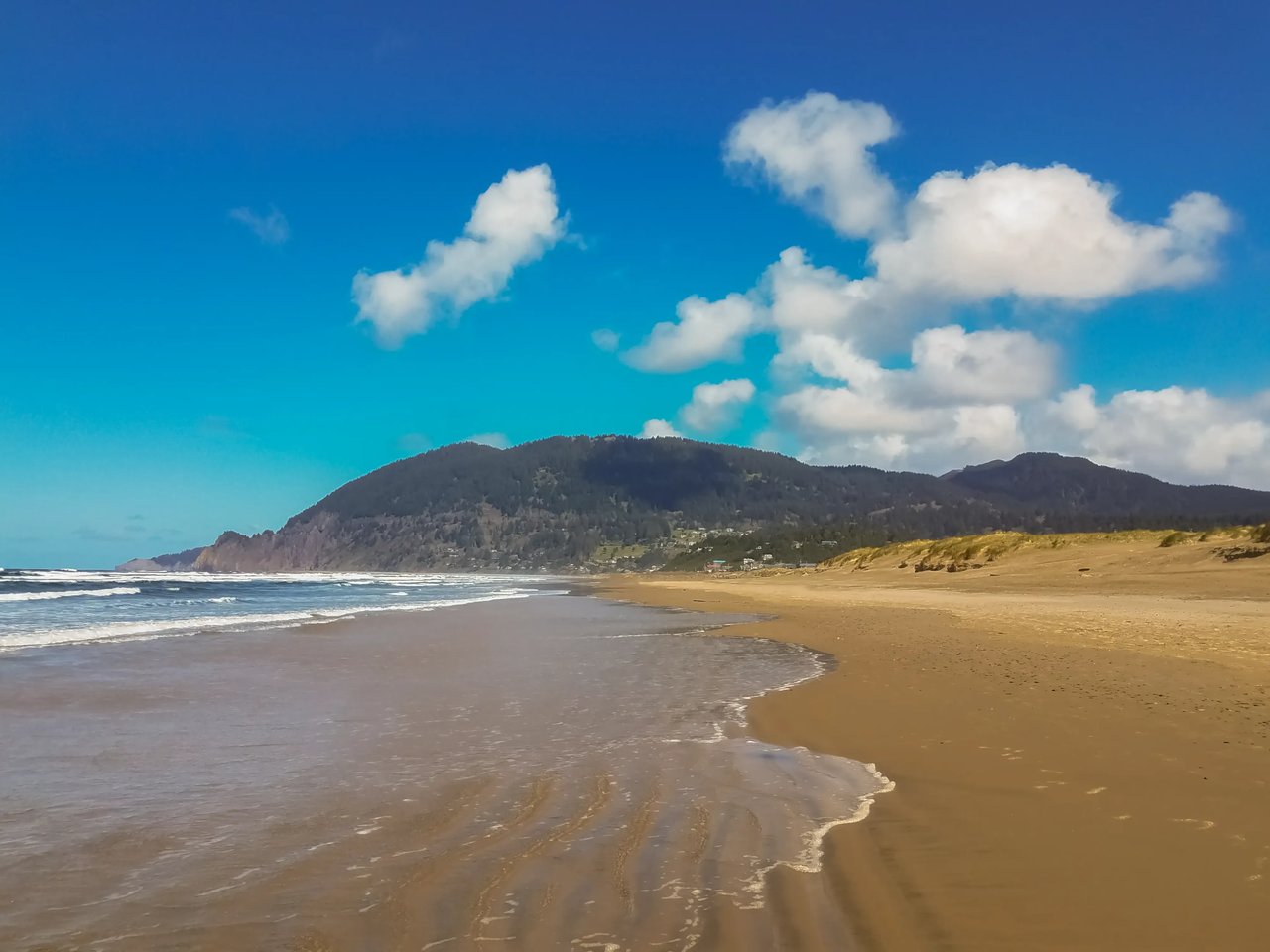 waves receding on a sandy beach with neahkanie mountain and puffy clouds in the distance