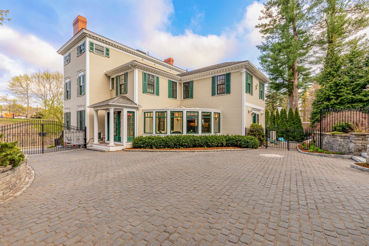 The house features numerous windows with dark green shutters, and prominent brick chimneys.