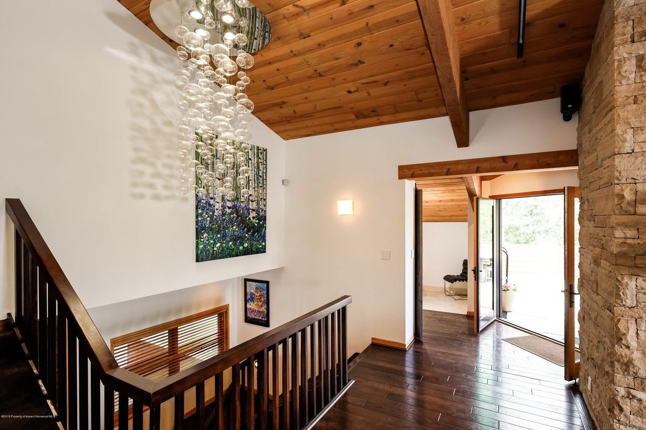 Entry hall with vaulted wood ceiling, cascading glass chandelier, dark wood stairs, and stone wall.