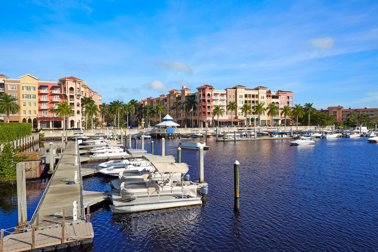 Waterfront marina with docked boats, palm-lined colorful buildings, and a canal.