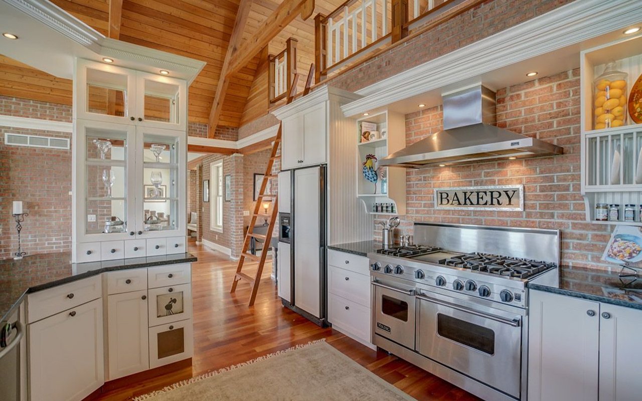 Kitchen with a stainless-steel range, exposed brick walls, vaulted wood ceiling, and ladder to an upper loft.