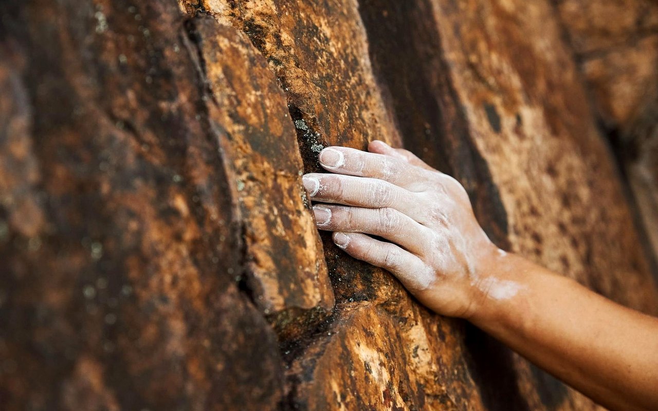 A chalk-covered hand grips a rugged rock climbing surface.