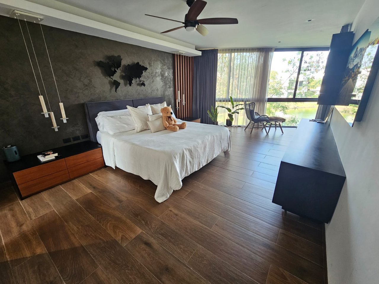 Modern bedroom with a white bed and large windows overlooking water and greenery.