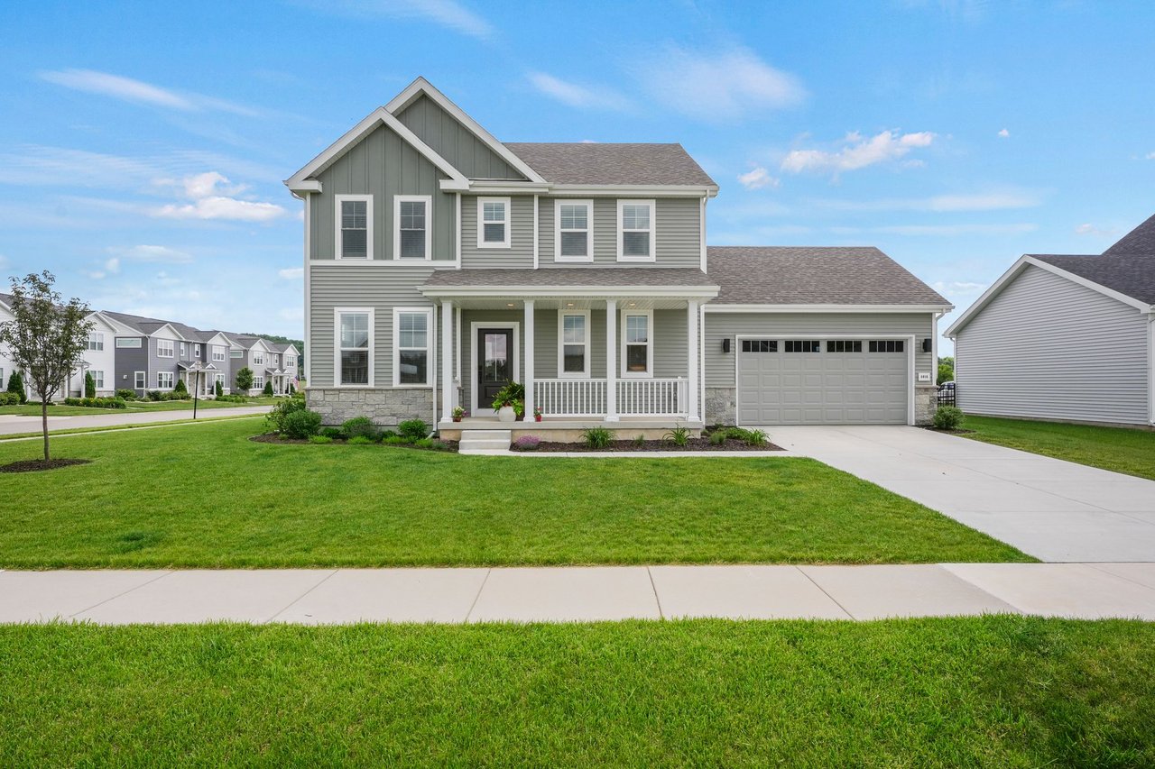 Front exterior of 8016 Laufenberg Boulevard, a two-story farmhouse-style home with a covered porch and two-car garage in Creek Crossing, Cross Plains, WI