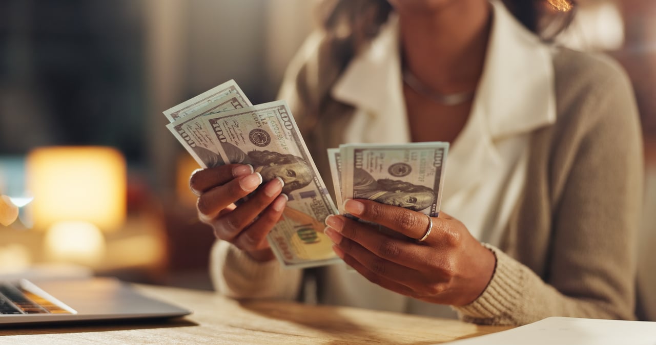 Close-up of woman counting $100 bills at a desk with a laptop, representing mortgage savings, lump sum payments, or refinancing options.