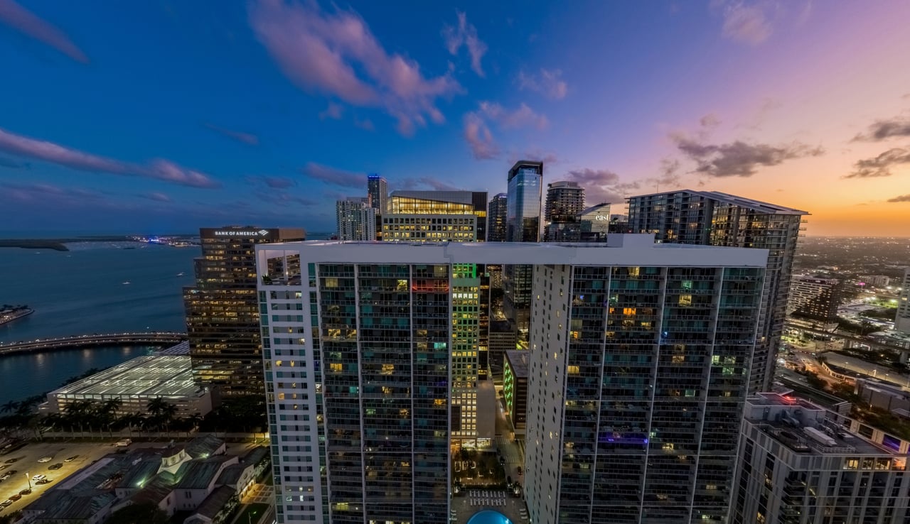 Brickell waterfront skyline at dusk, with illuminated high-rises and water beside the buildings.