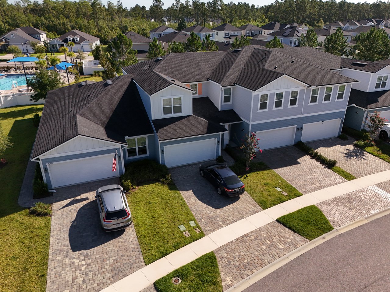 Aerial view of attached homes with garages and driveways beside a community swimming pool.