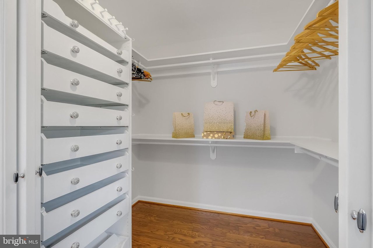 Walk-in closet with built-in drawers, wraparound shelves, wooden hangers, and hardwood flooring.