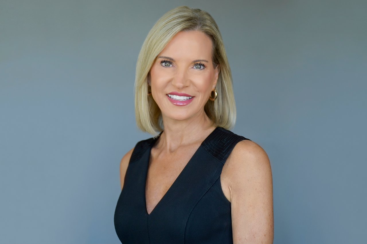 Amy Carpenter, real estate agent, smiling in a black sleeveless top against a blue-gray background.