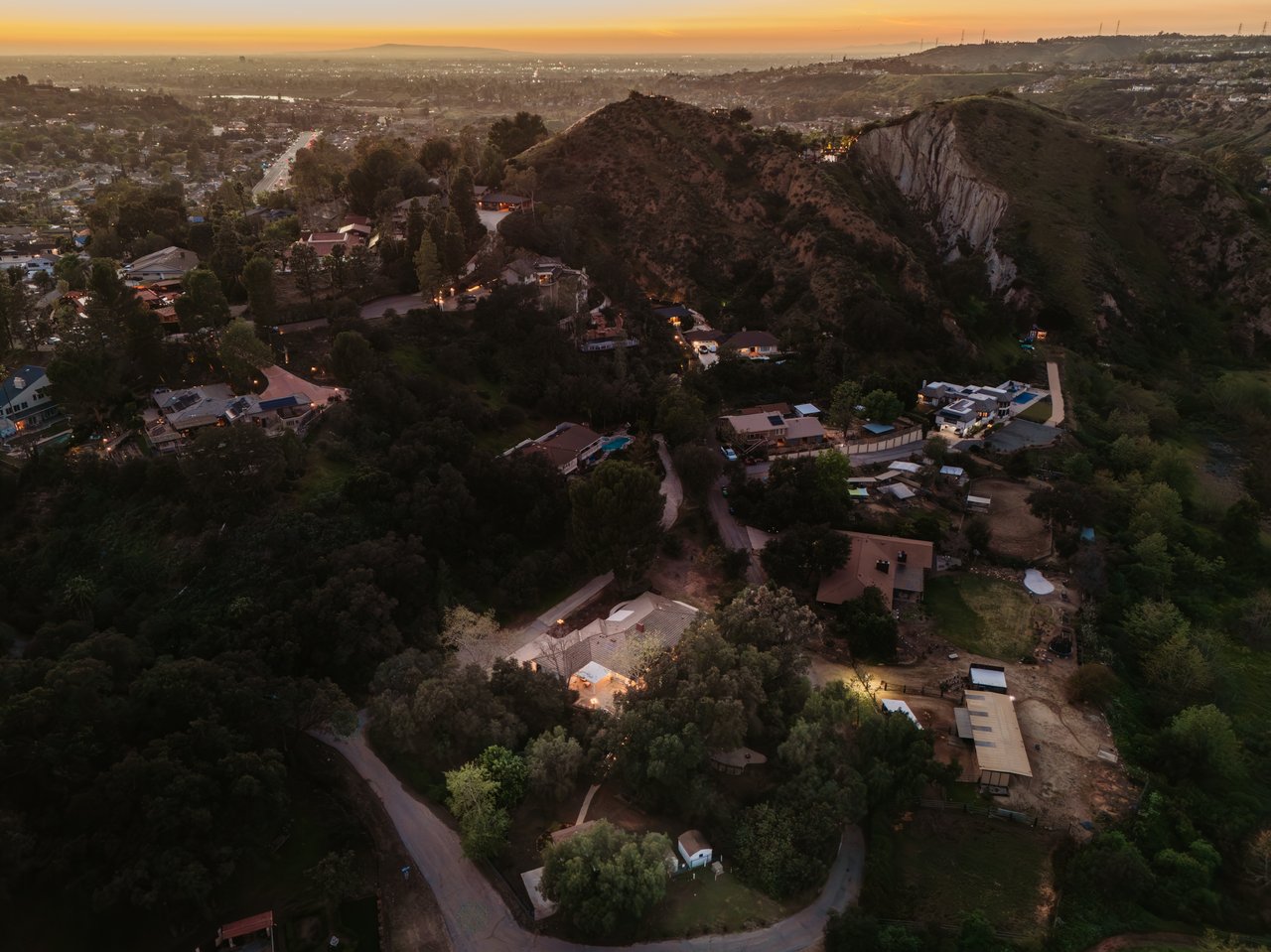 Aerial view of Orange Park Acres homes among wooded hills at dusk, with a rocky ridge and sunset sky.