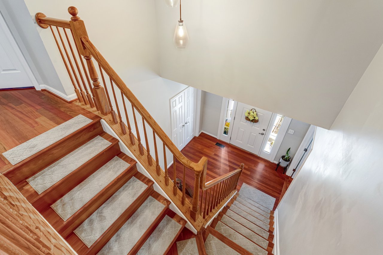 Wooden staircase overlooking a hardwood entry foyer with a white front door.