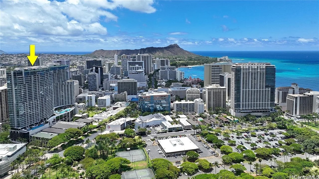 Aerial view of Waikiki with a yellow arrow marking a high-rise, ocean and Diamond Head beyond.
