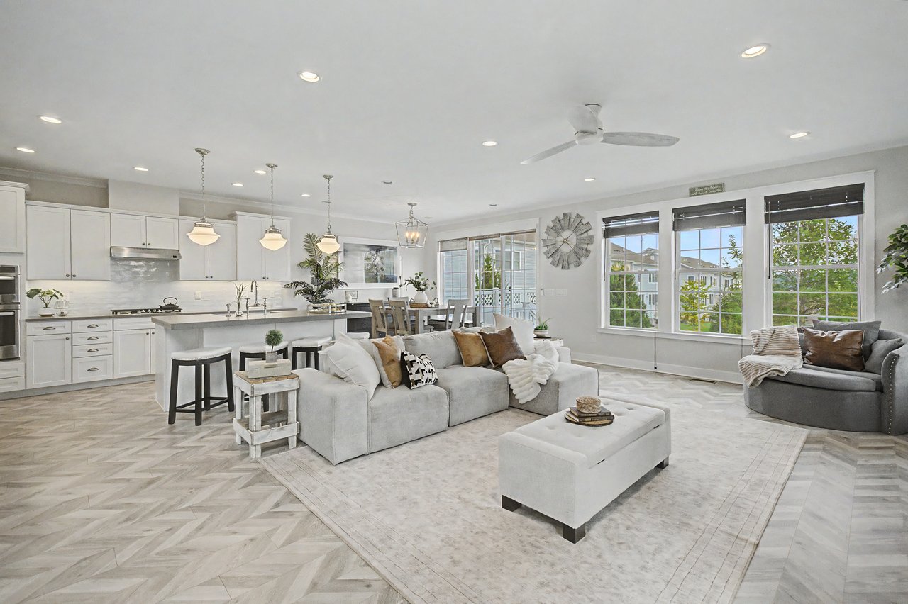 Open-plan living room and kitchen with a large island, light furnishings, and expansive windows.