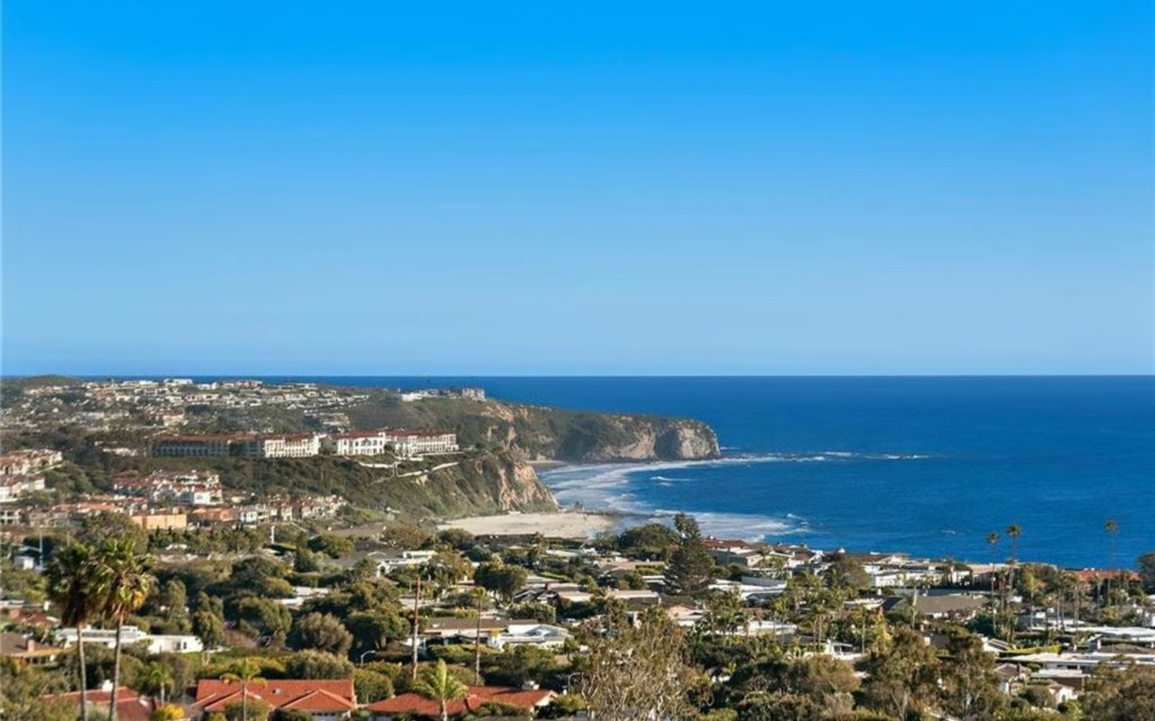 Laguna Beach coastline with a sandy cove, rugged headland, and Pacific Ocean beyond nearby homes.