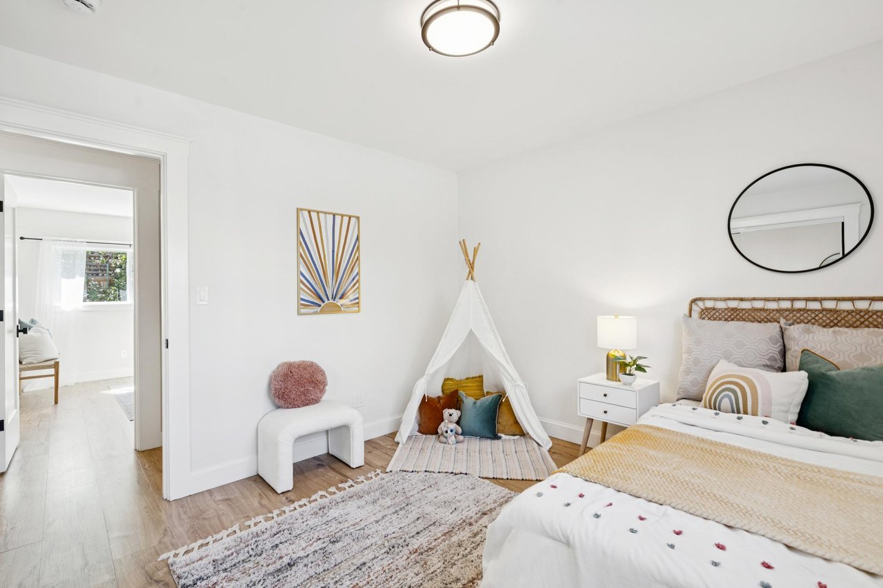 Staged bedroom with a woven headboard, oval mirror, and small play tent beside the bed.
