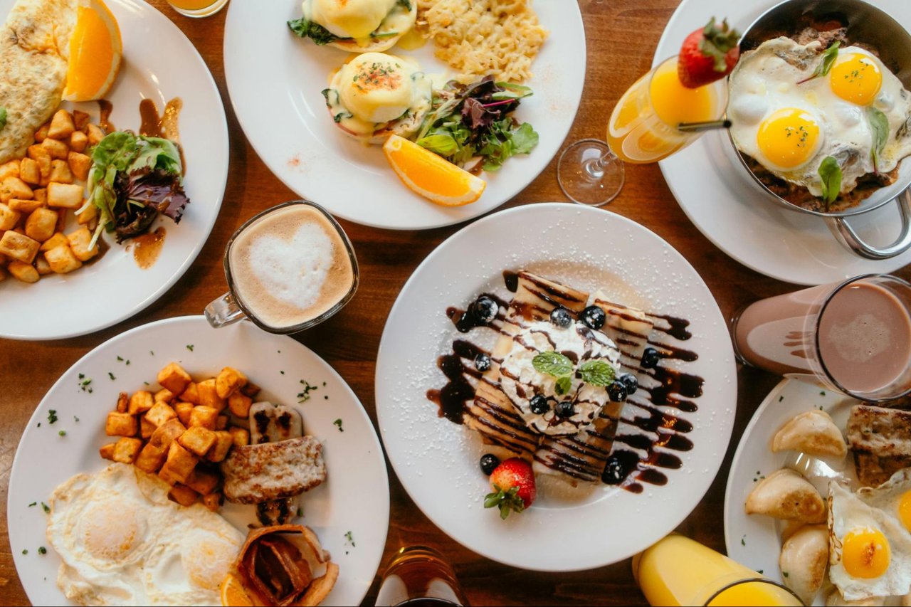 Breakfast spread with eggs, potatoes, pancakes with berries, coffee, and orange juice.