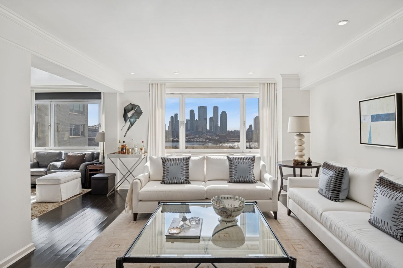 Living room with white sofas and a glass coffee table, overlooking the city skyline.
