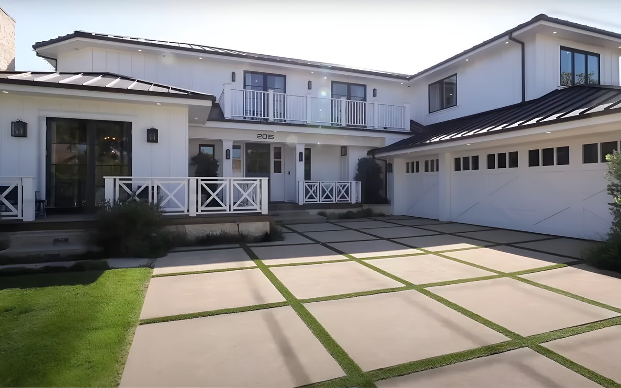 A large, modern white house with a two-car garage, a blue front door, and a driveway with green grass growing.