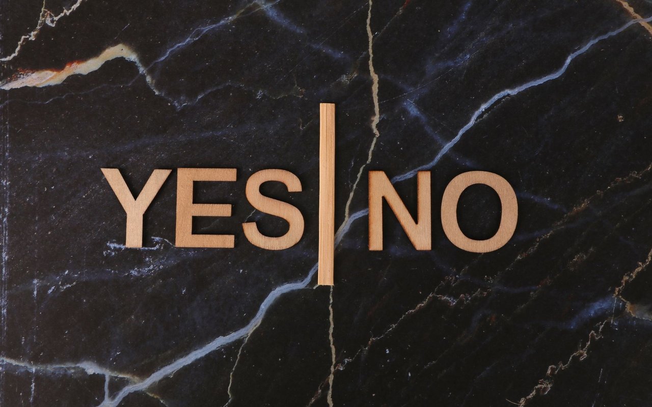 Wooden “YES” and “NO” letters separated by a vertical bar on dark stone.