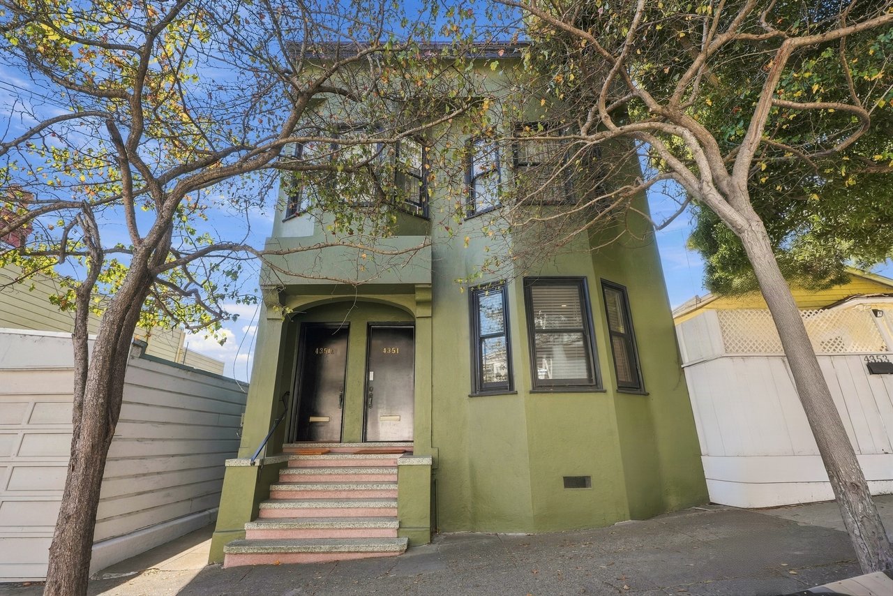 Green two-story home with paired entry doors, front steps, and mature trees.