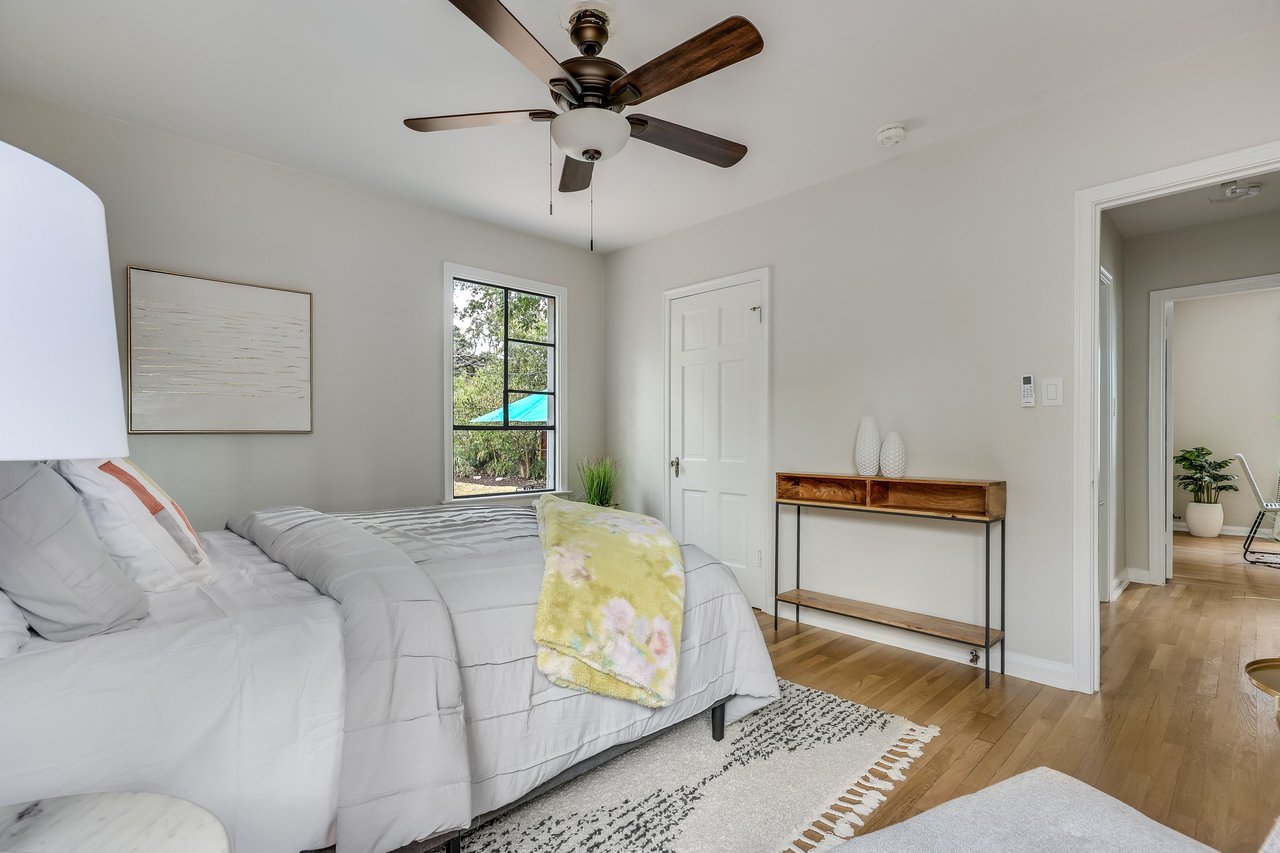 Staged bedroom with a white bed, floral throw, ceiling fan, and wood floors.