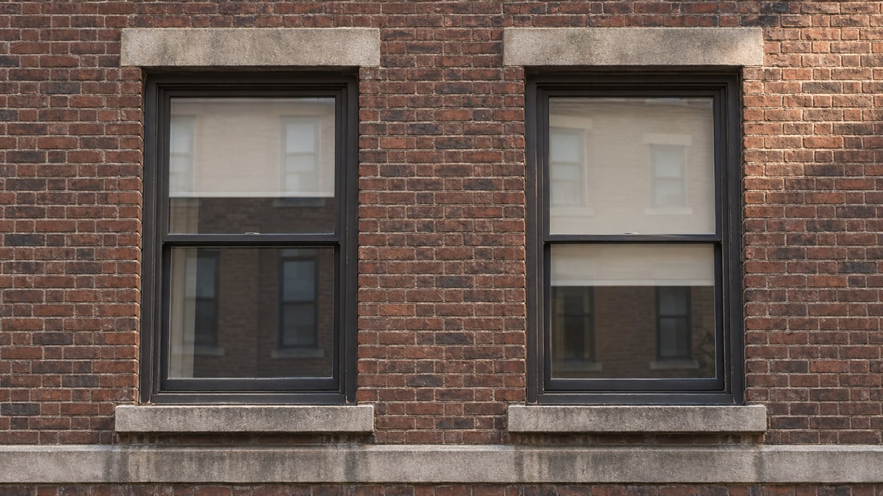 Two bronze-framed apartment windows set in russet brick with weathered limestone lintels and sills.
