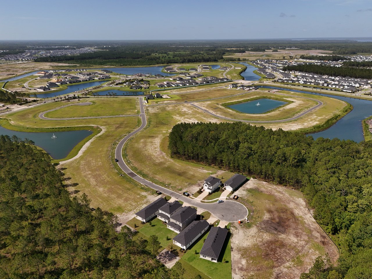 Aerial view of a residential community with ponds, wooded areas, and homes among undeveloped lots.