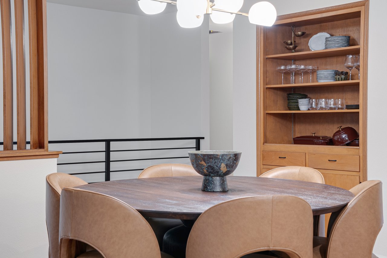 Dining area with a dark table, tan chairs, globe pendant light, and built-in wooden dish shelves.