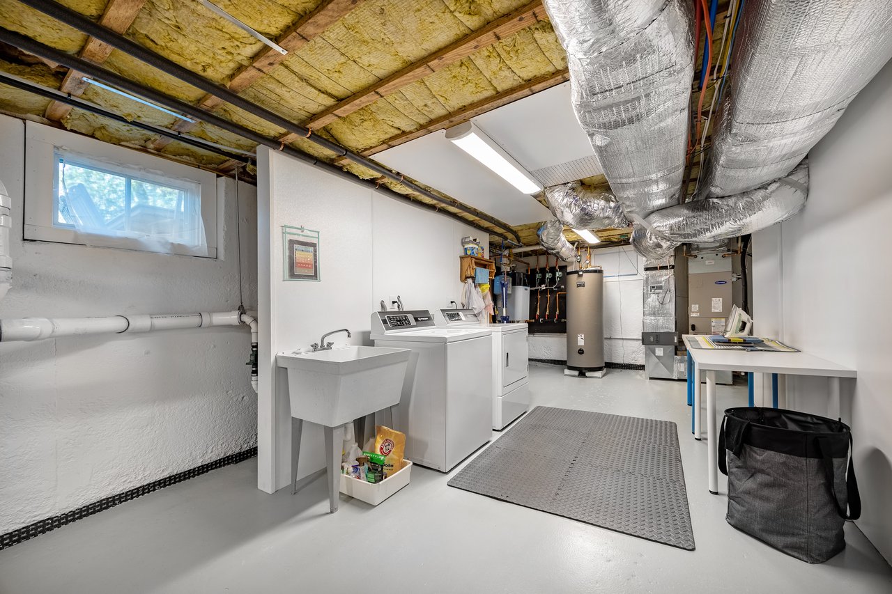 Basement laundry room with washer, dryer, utility sink, and exposed ductwork.