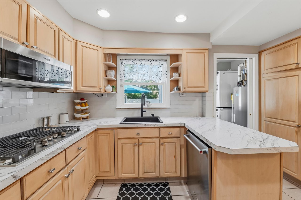 Kitchen with light wood cabinetry, white counters, gas cooktop, and sink beneath a window.