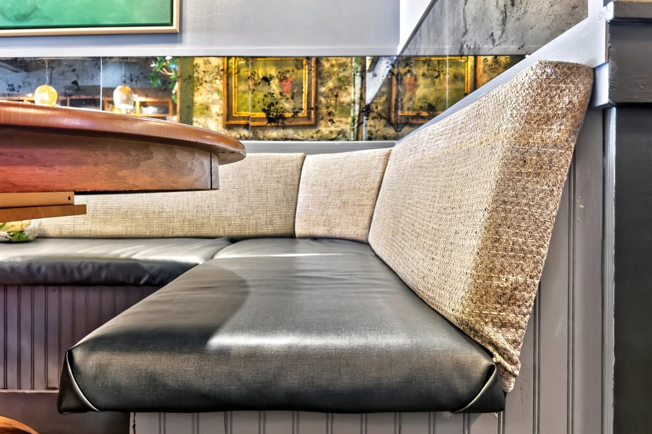Restaurant booth with dark gray cushions, textured beige backrests, and a wooden table.
