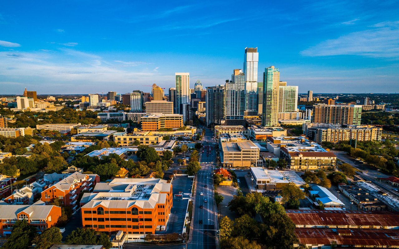Aerial view of downtown Austin’s high-rise skyline and tree-lined streets in warm evening light.