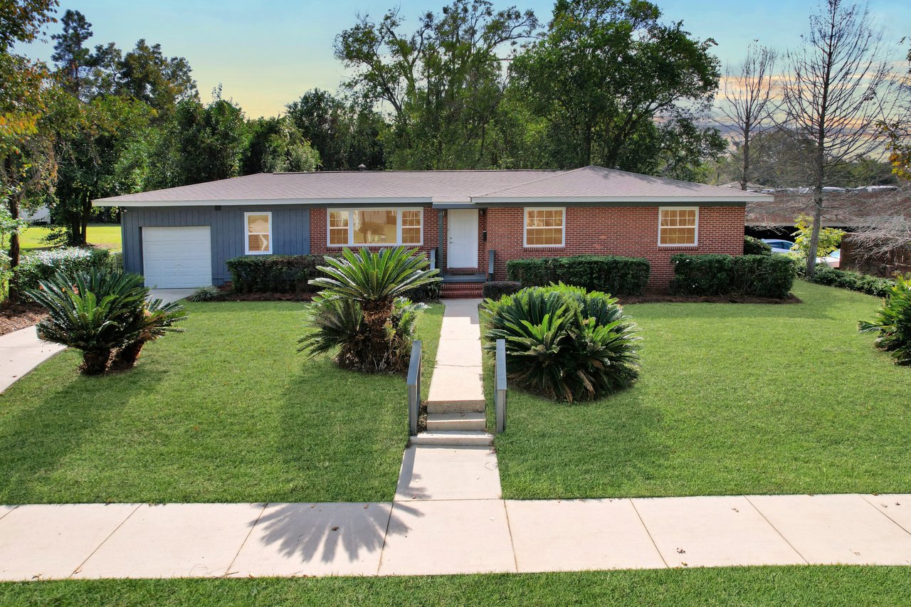 A brick house surrounded by a lush lawn and palm trees, showcasing a serene and inviting outdoor environment.