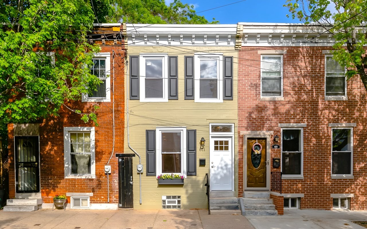 Philadelphia row houses with a tan-sided home and dark shutters between red-brick neighbors.
