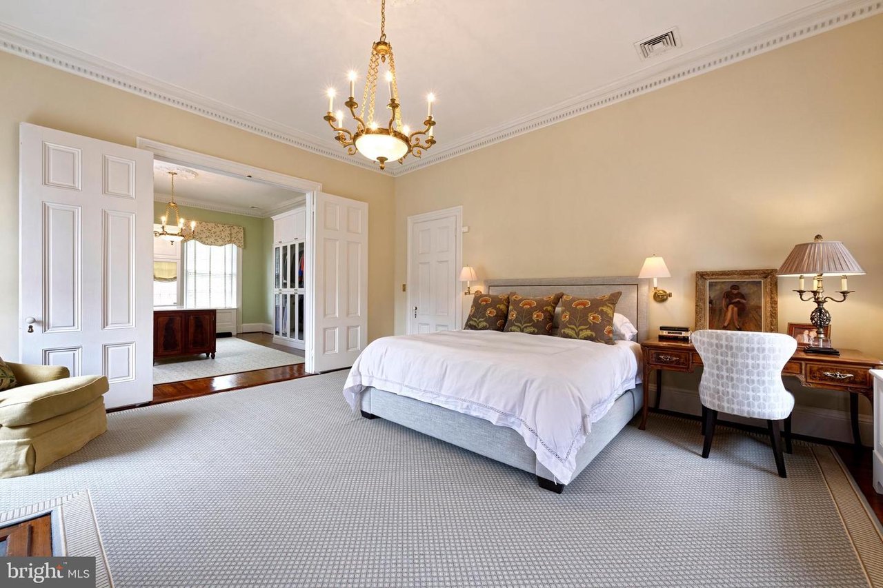Bedroom with a white bed, brass chandelier, patterned carpet, and open double doors to an adjoining room.