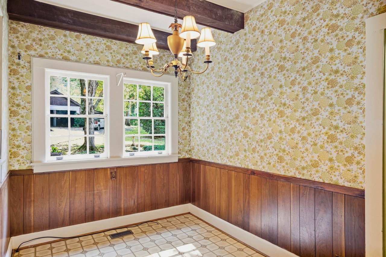 Empty room with floral wallpaper, wood wainscoting, tiled floor, and a chandelier.
