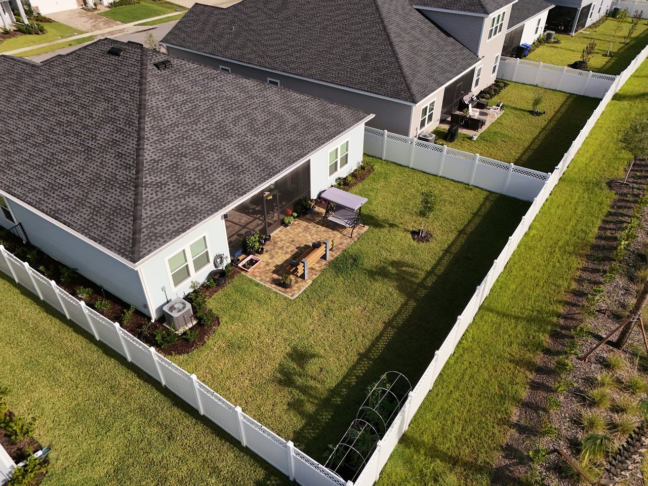 Aerial view of fenced home backyards with screened patios and a paver seating area.